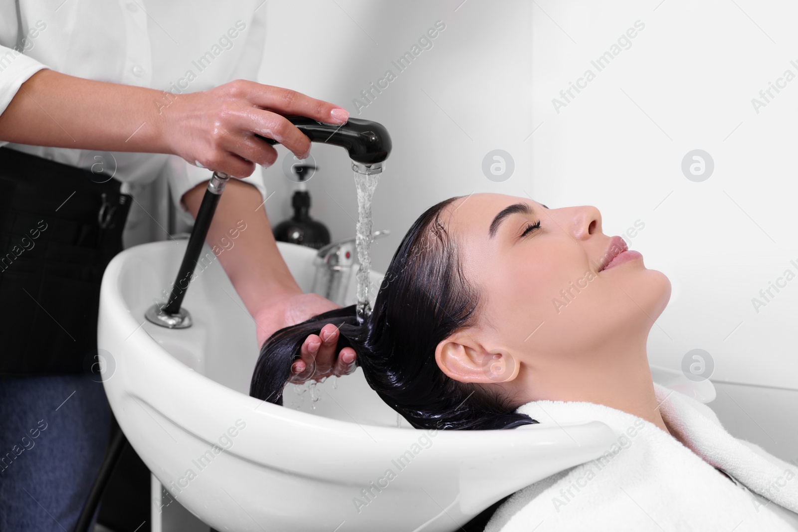 Photo of Professional hairdresser washing woman's hair in beauty salon, closeup