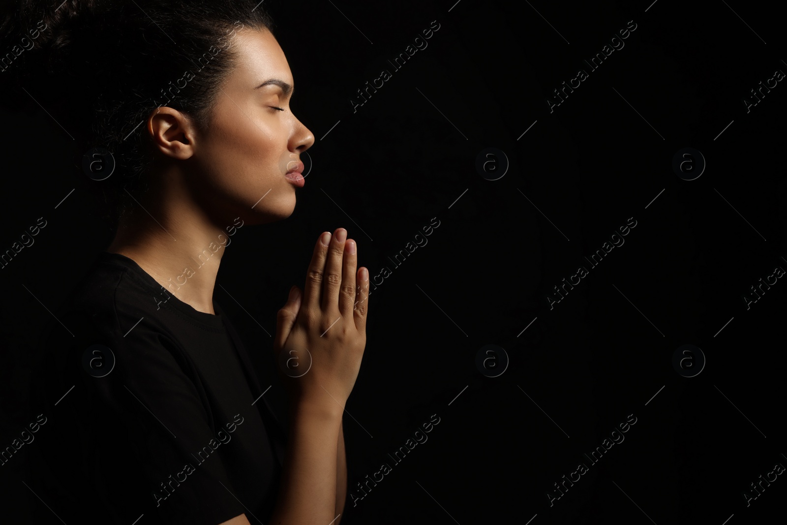 Photo of African American woman with clasped hands praying to God on black background. Space for text