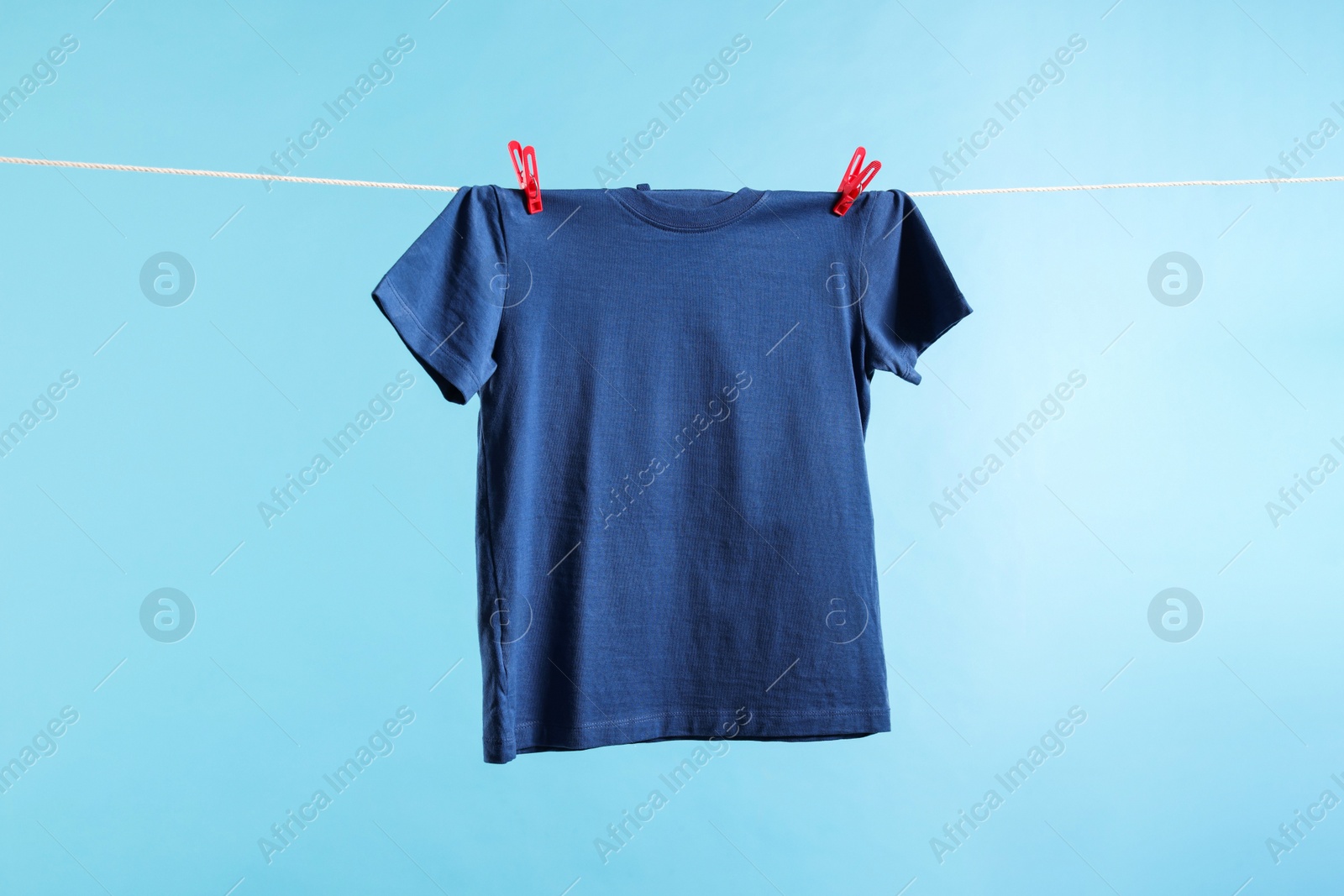 Photo of One t-shirt drying on washing line against light blue background