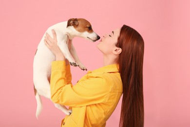 Photo of Woman kissing her cute Jack Russell Terrier dog on pink background