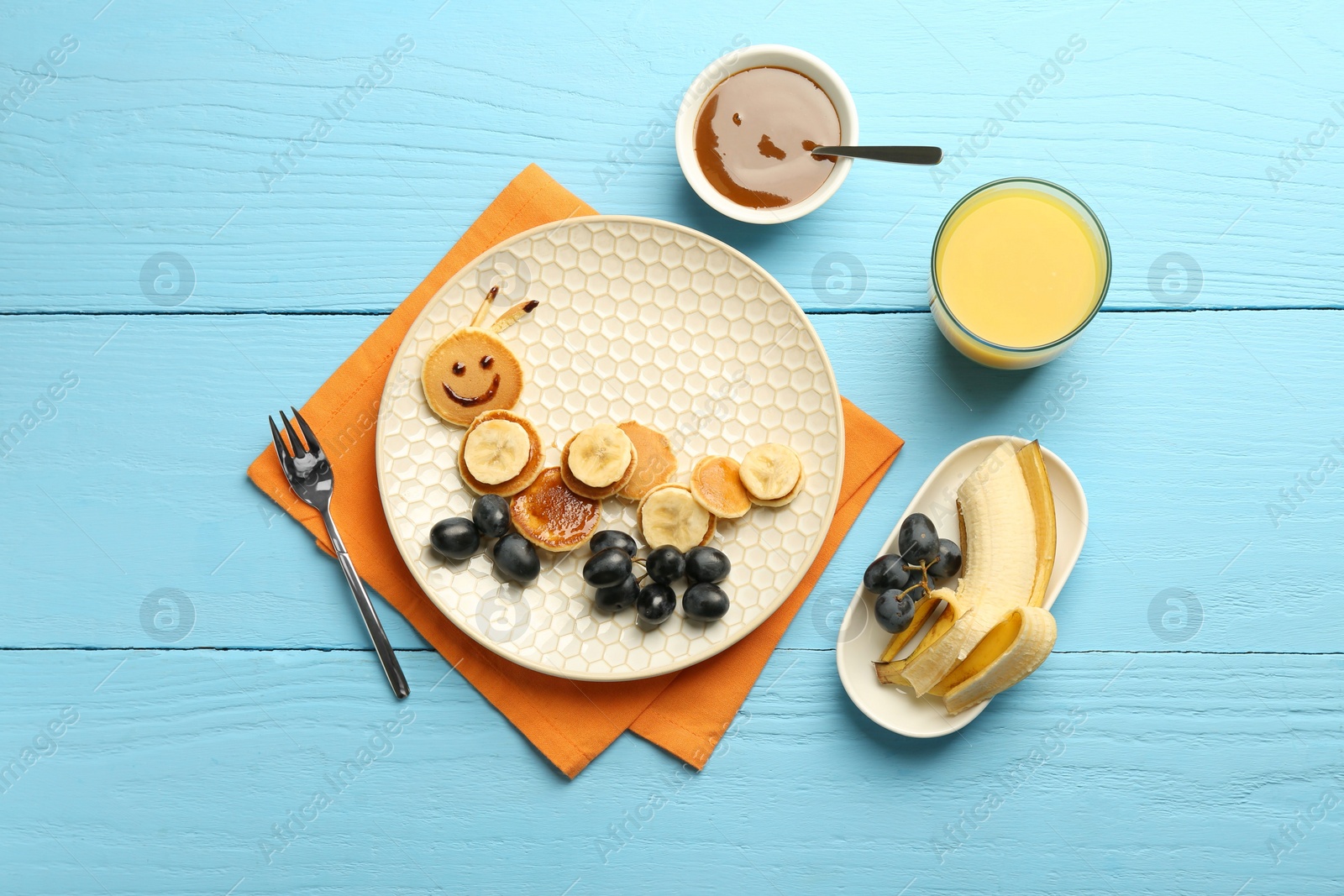 Photo of Creative serving for kids. Plate with cute caterpillar made of pancakes, grapes and banana on light blue wooden table, flat lay