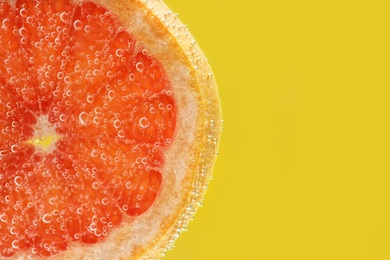 Slice of grapefruit in sparkling water on yellow background, closeup with space for text. Citrus soda