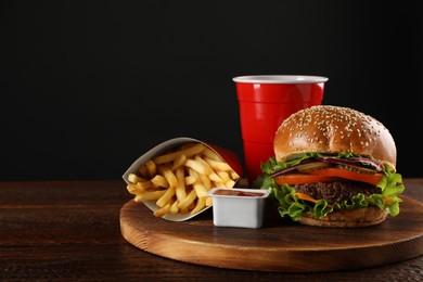 Photo of Burger, French fries, ketchup and refreshing drink on wooden table, space for text. Fast food