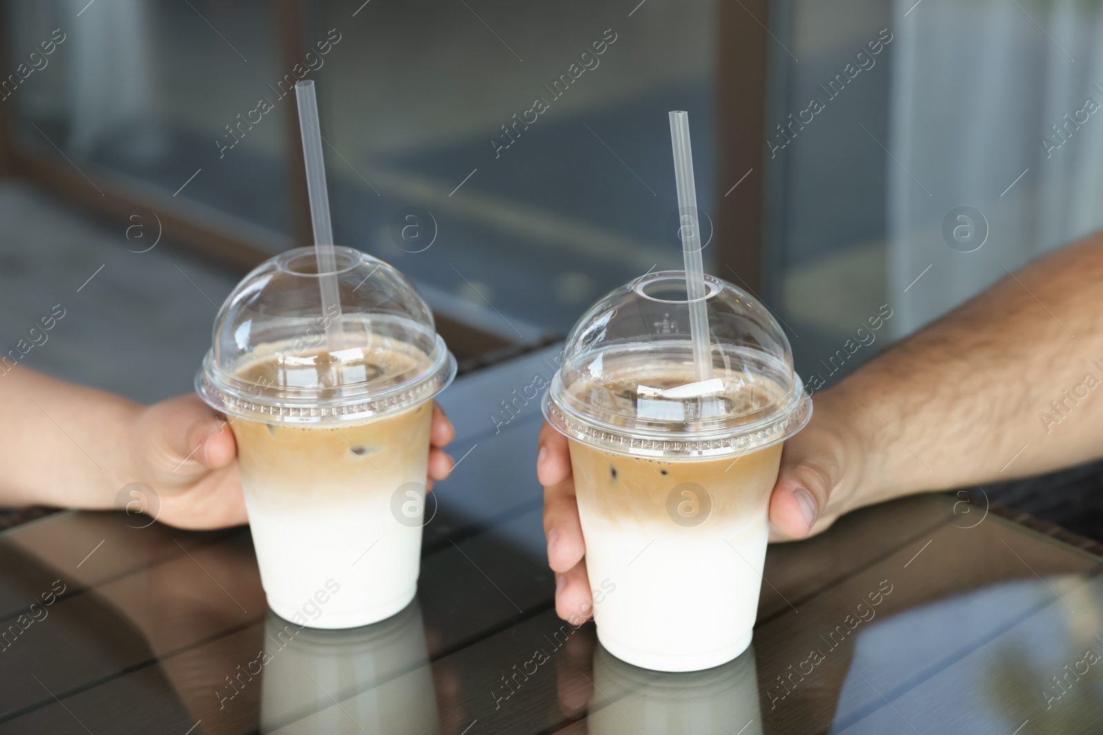 Photo of Man and woman with plastic takeaway cups of delicious iced coffee at table in outdoor cafe, closeup