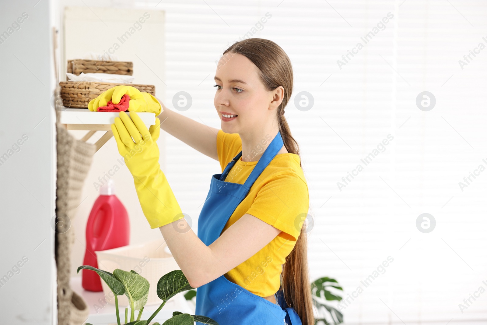 Photo of Woman cleaning shelf with rag at home, space for text