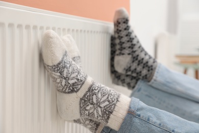 Photo of Couple warming legs on heating radiator indoors, closeup