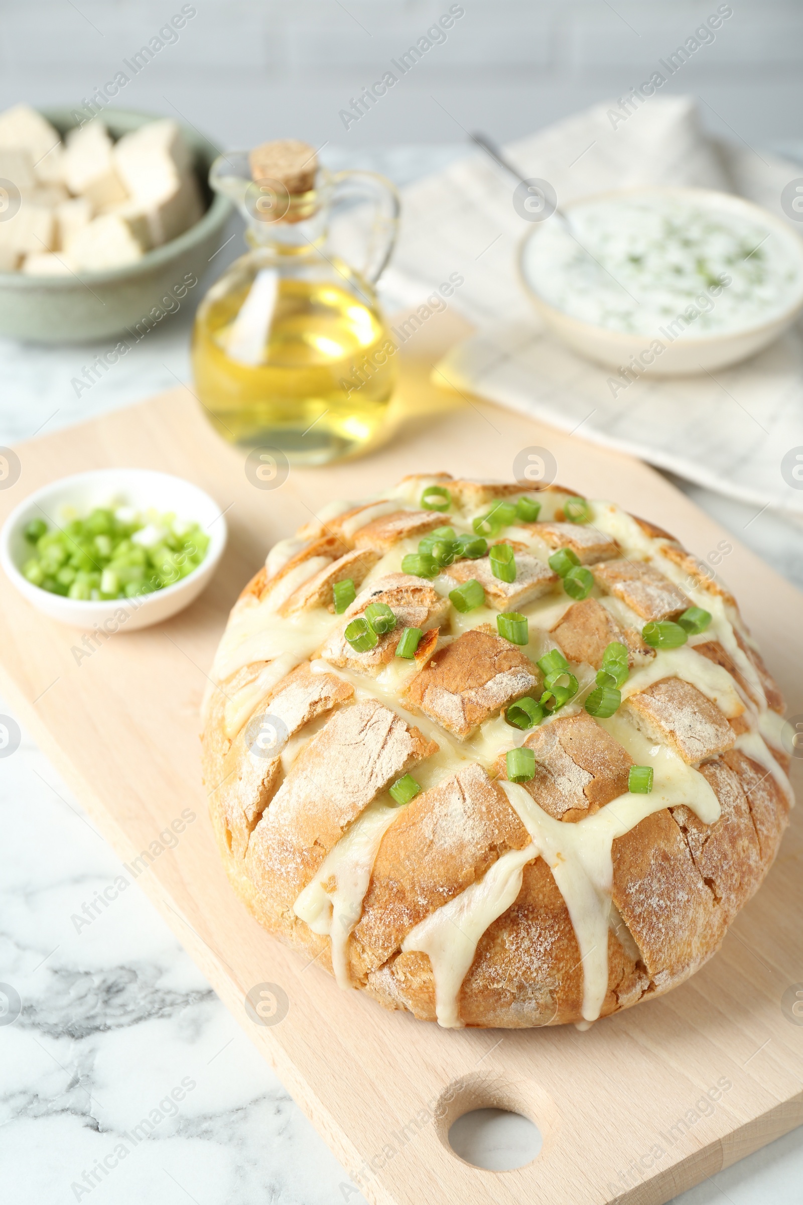 Photo of Freshly baked bread with tofu cheese and green onion on white marble table