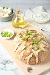 Photo of Freshly baked bread with tofu cheese and green onion on white marble table