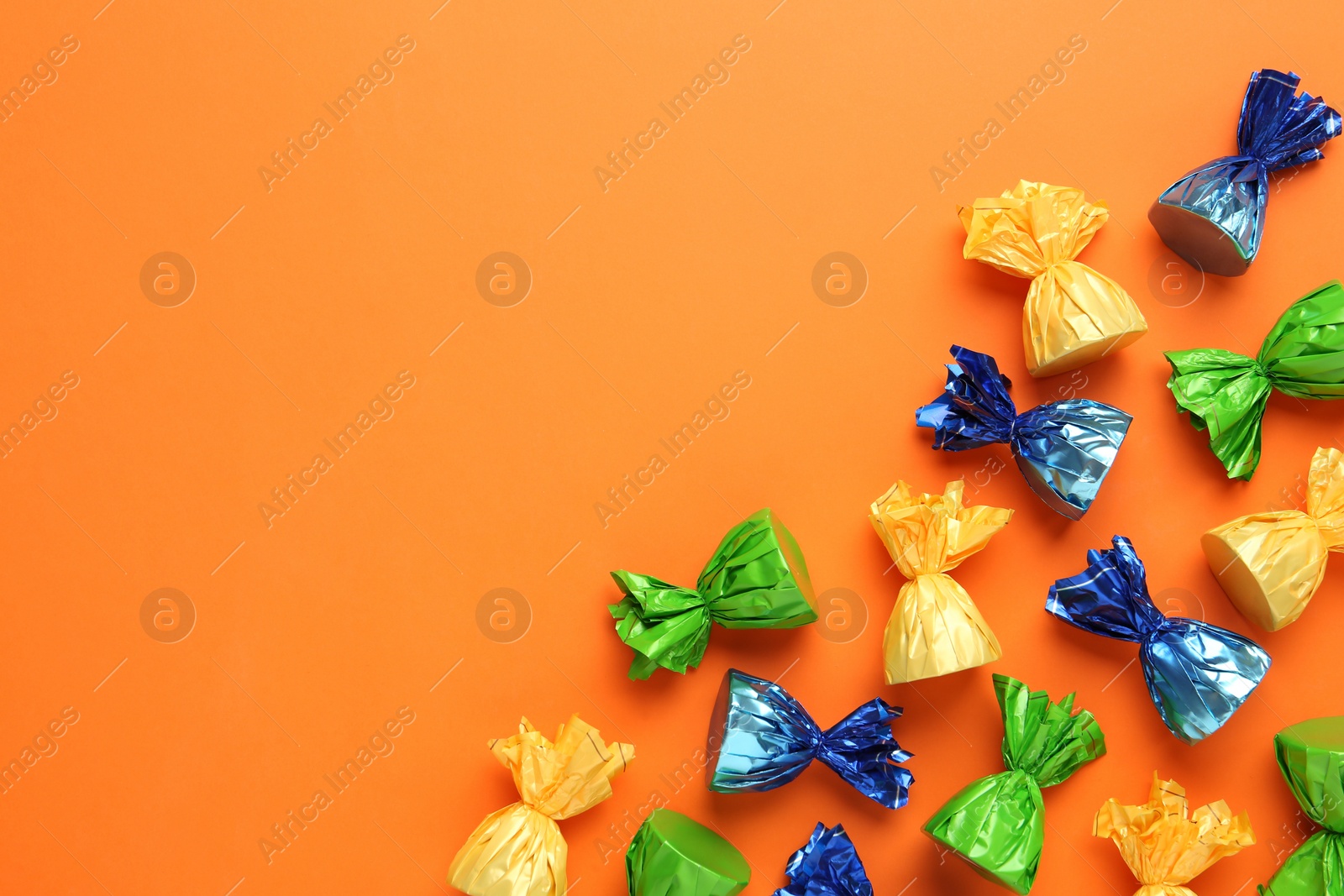 Photo of Many candies in colorful wrappers on orange background, flat lay. Space for text