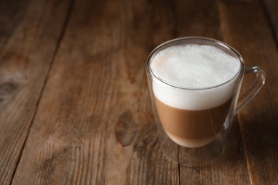 Photo of Hot coffee with milk in glass cup on wooden table. Space for text