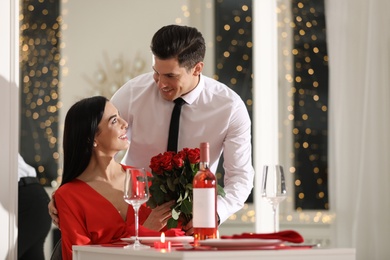 Man presenting roses to his beloved woman in restaurant. Romantic Valentine's day dinner
