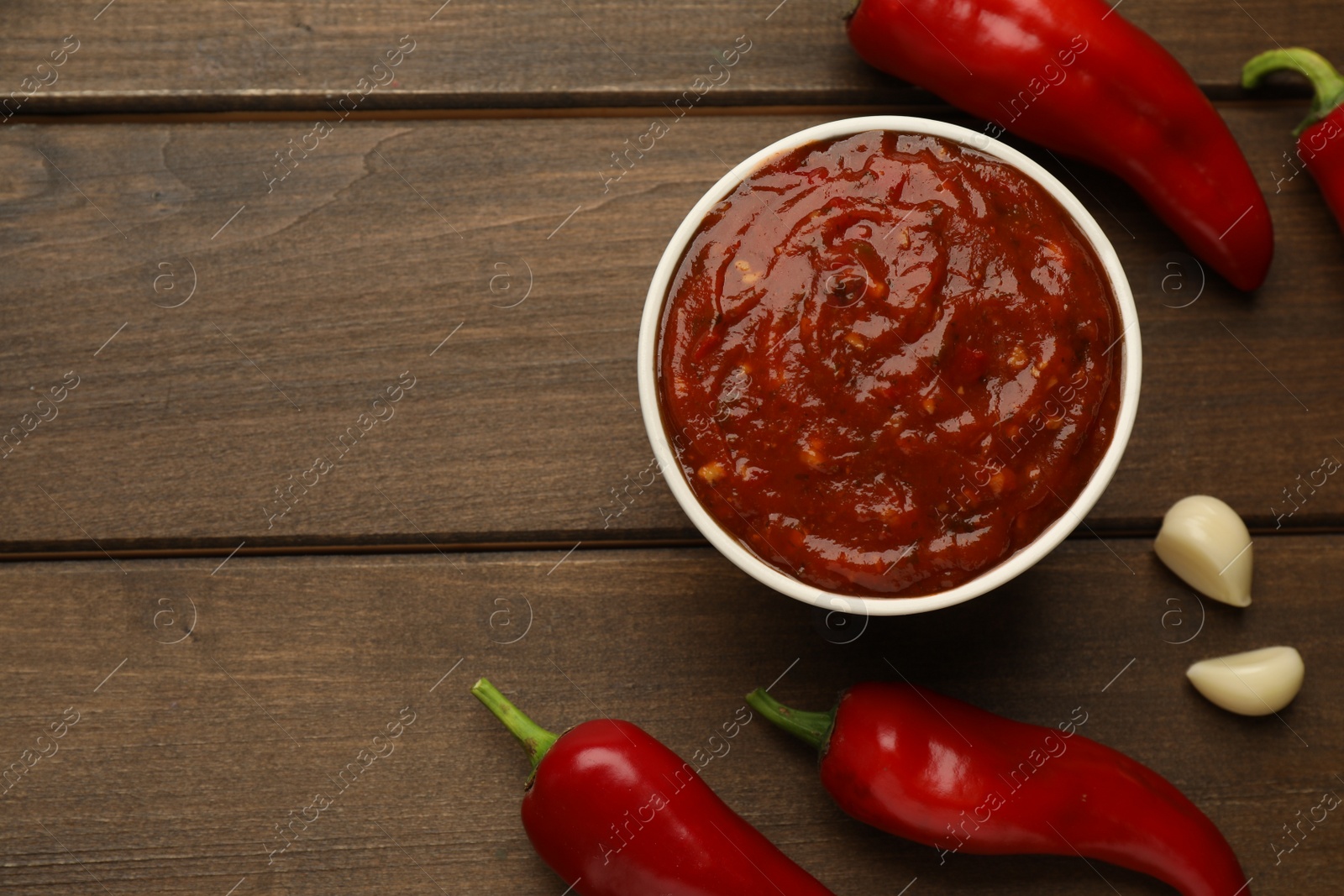 Photo of Delicious adjika sauce in bowl and ingredients on wooden table, flat lay. Space for text