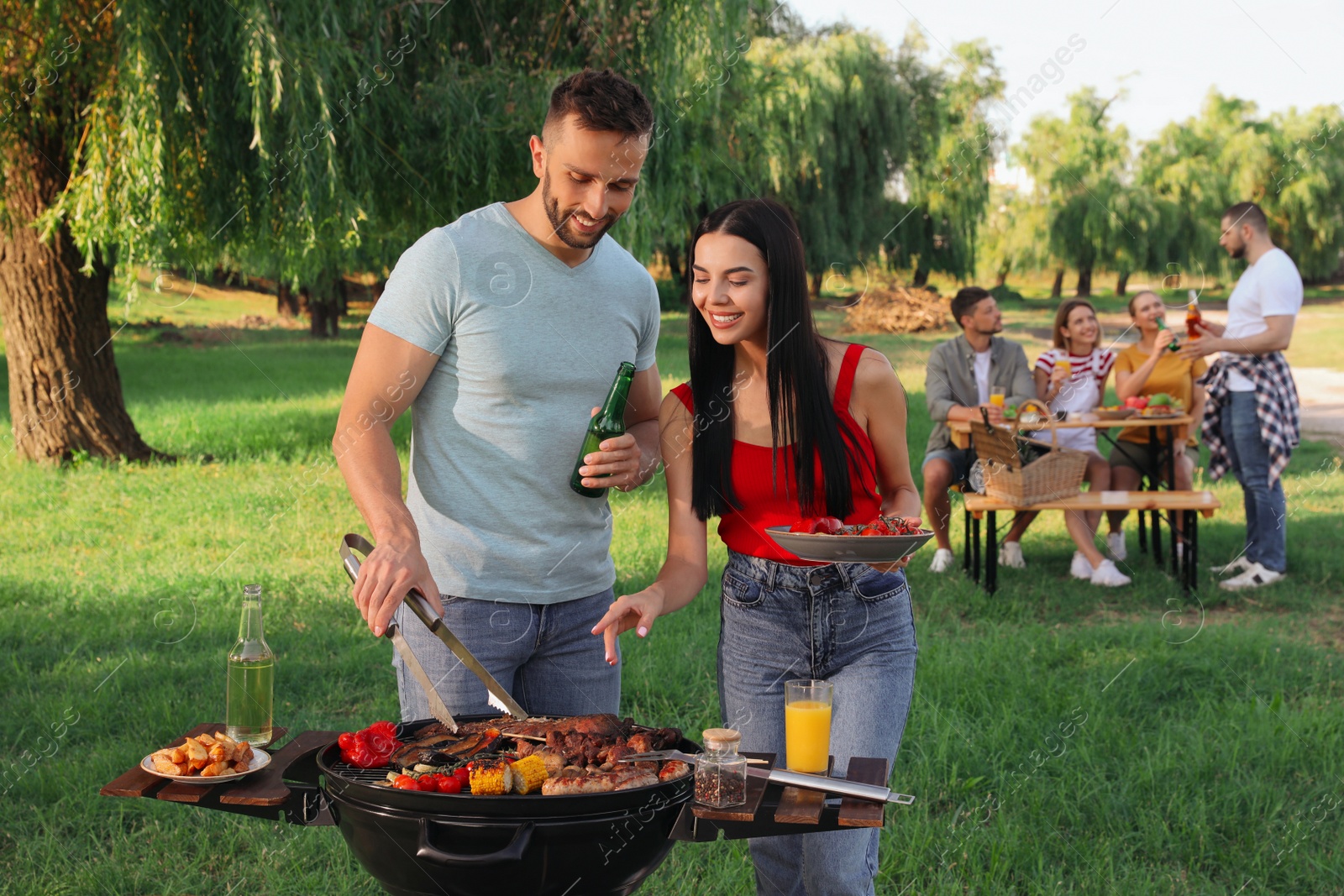 Photo of Happy friends cooking meat and vegetables on barbecue grill in park