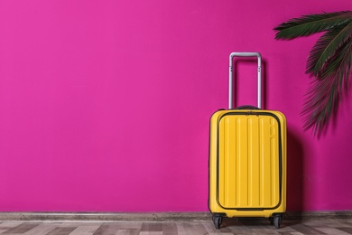 Photo of Bright yellow suitcase and palm branches near color wall indoors