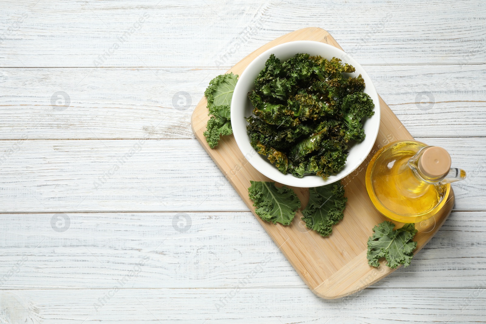 Photo of Tasty baked kale chips on white wooden table, top view. Space for text