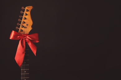 Photo of Guitar with red bow on black background, space for text. Christmas music