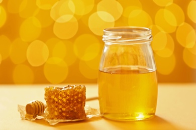 Photo of Jar with honey and fresh comb on table against blurred background