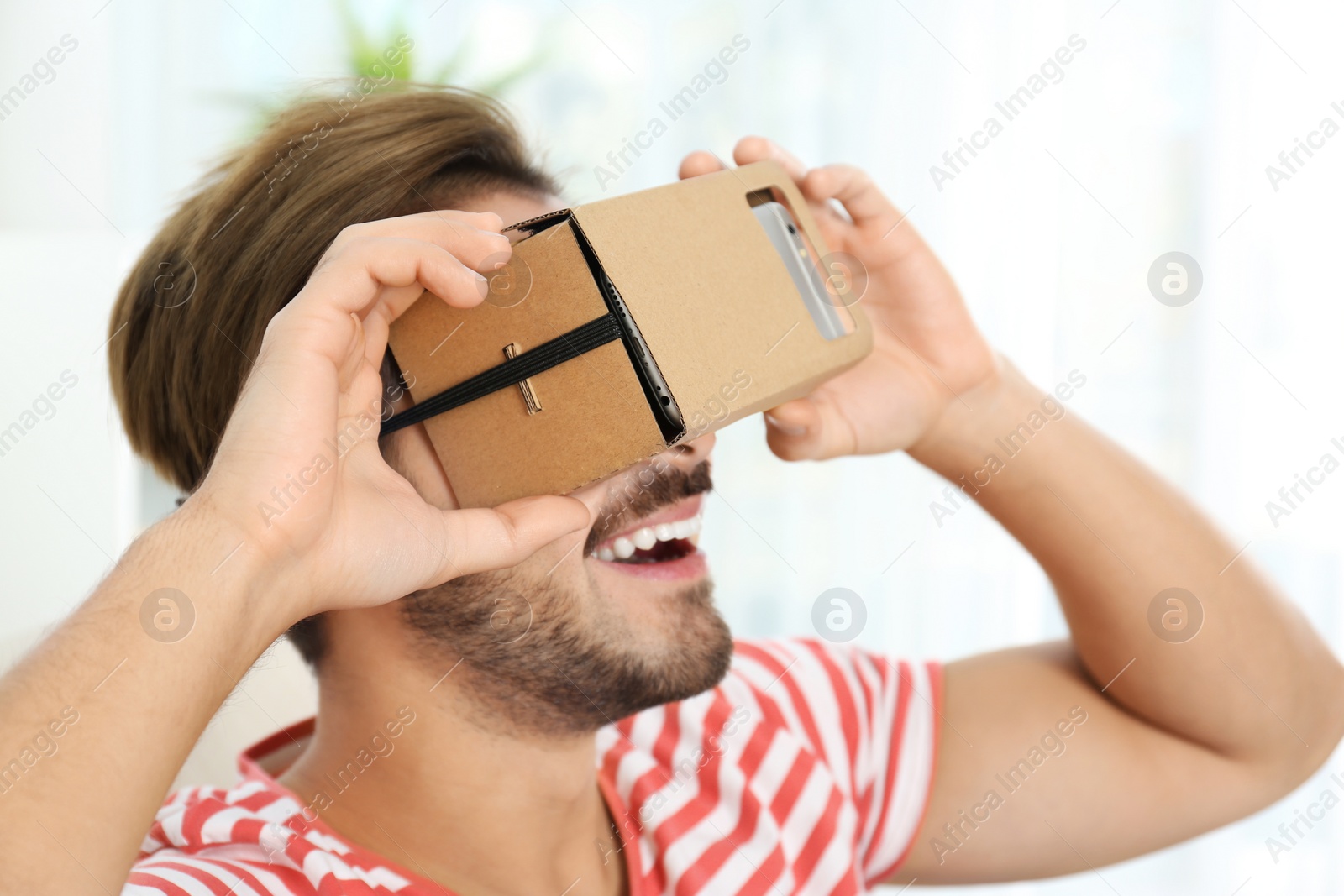 Photo of Young man using cardboard virtual reality headset at home