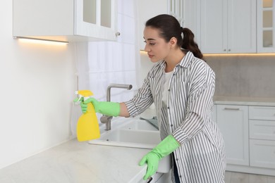 Photo of Woman with spray bottle cleaning wall in kitchen