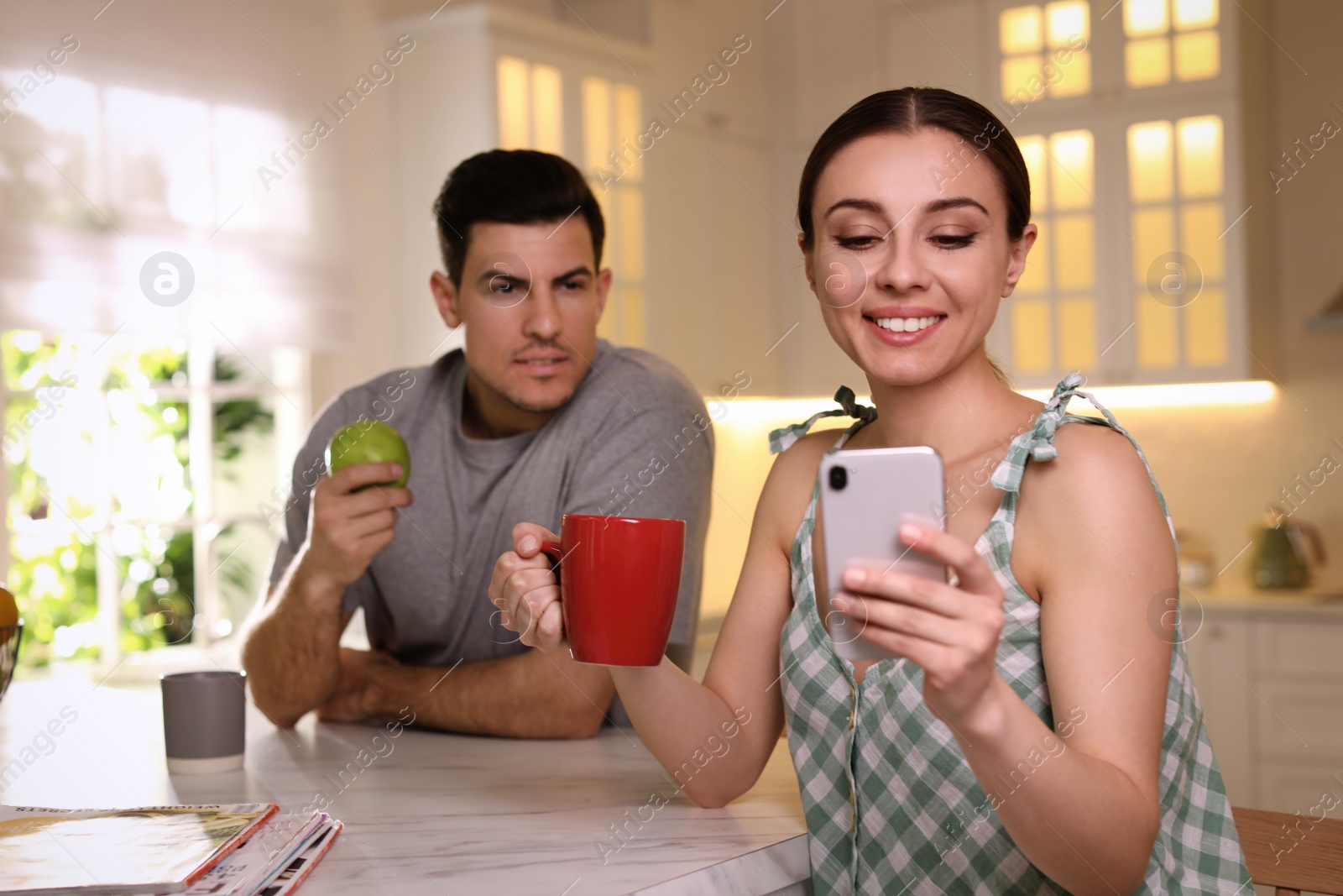 Photo of Distrustful man peering into girlfriend's smartphone at home. Jealousy in relationship