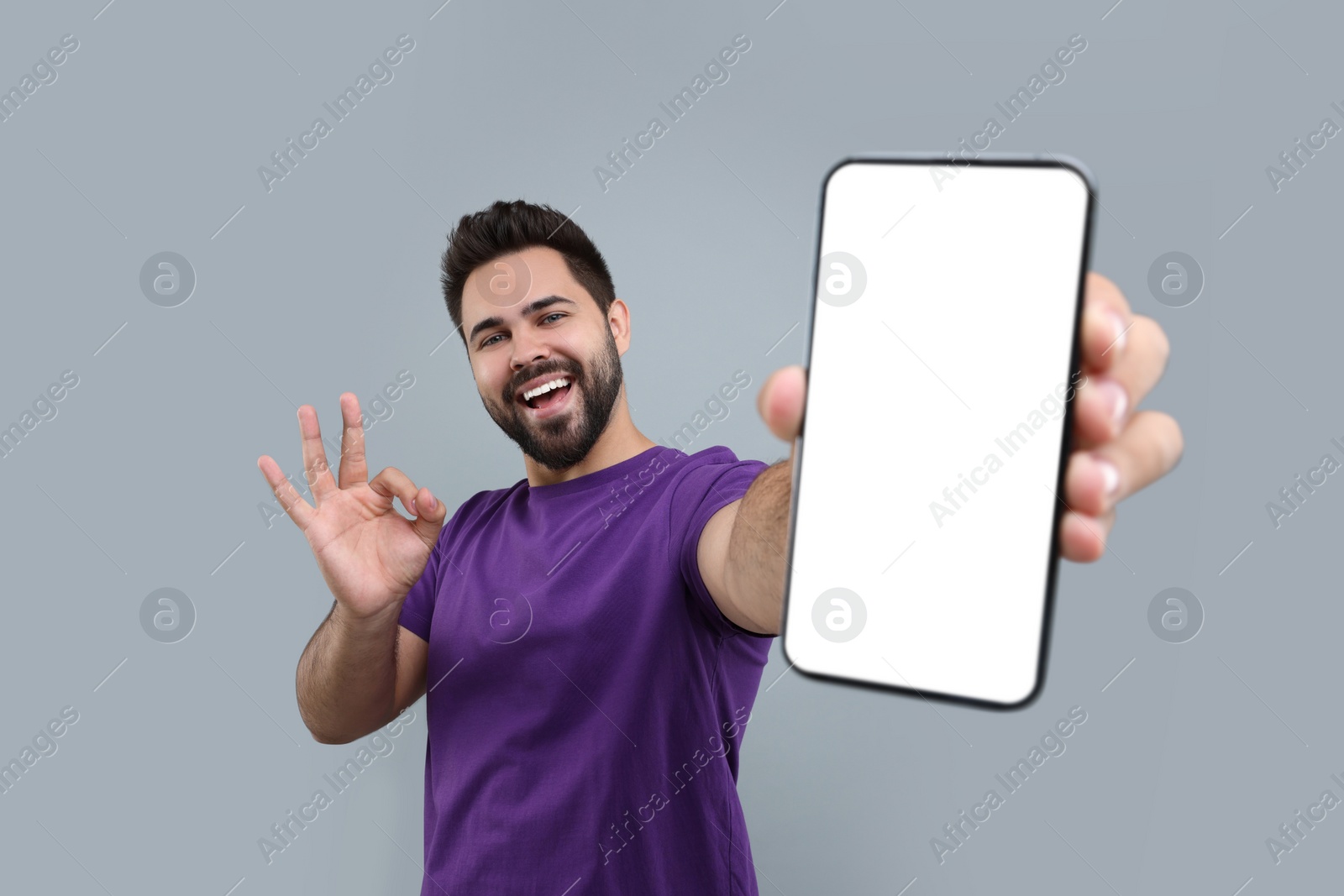 Photo of Young man showing smartphone in hand and OK gesture on light grey background