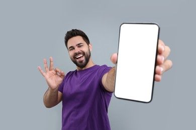 Photo of Young man showing smartphone in hand and OK gesture on light grey background