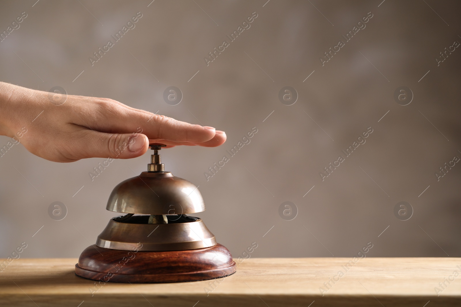 Photo of Woman ringing hotel service bell at wooden table, closeup. Space for text