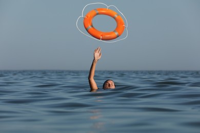 Image of Drowning woman with raised hand getting lifebelt in sea