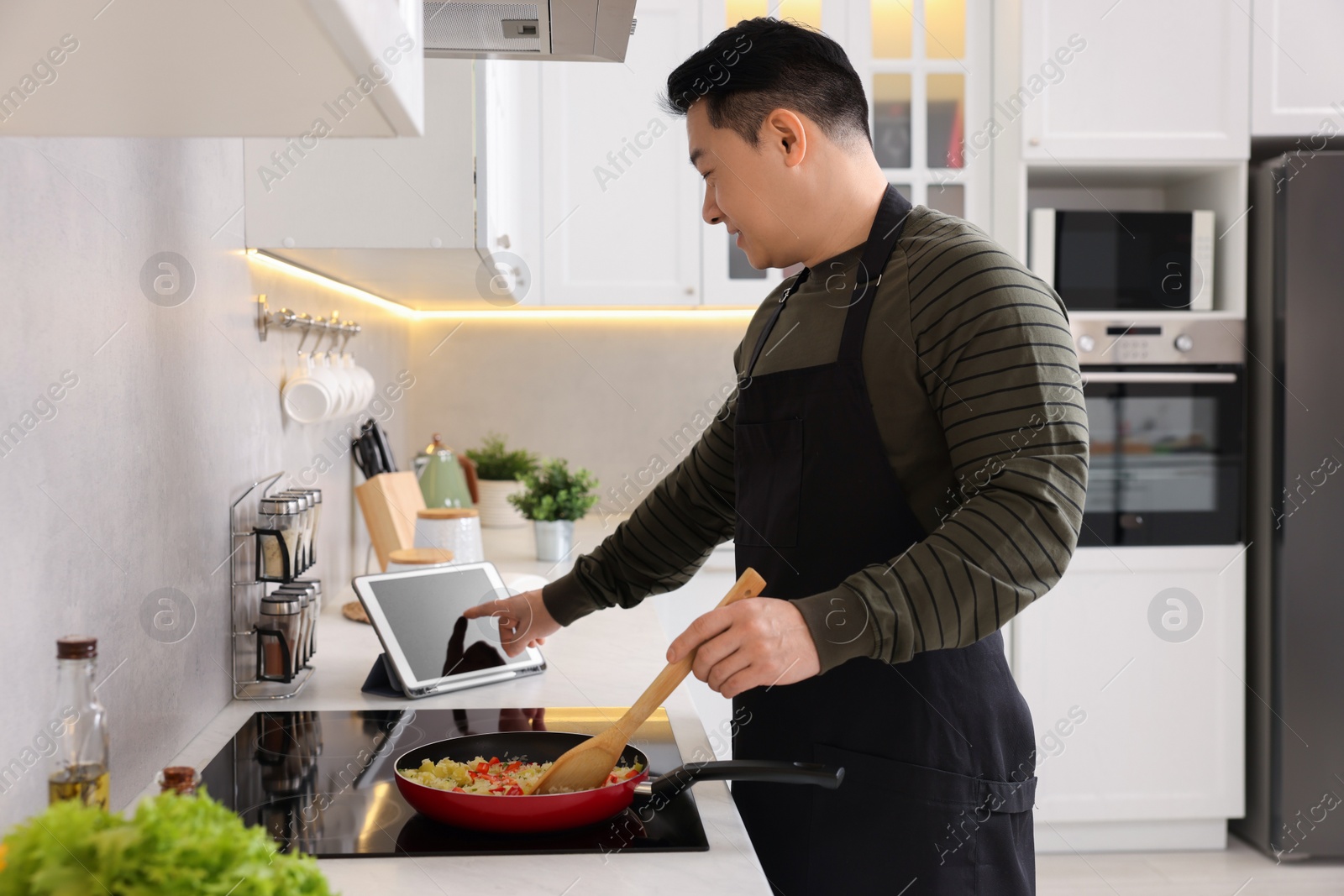Photo of Man using tablet while cooking in kitchen