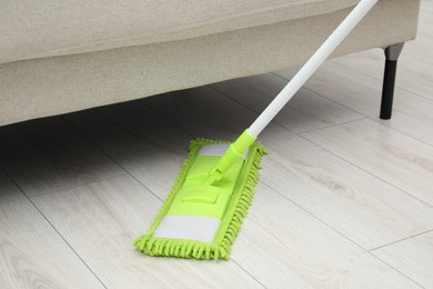 Photo of Cleaning white parquet floor under sofa with mop, closeup