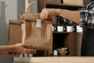Photo of Worker giving paper bags to customer in cafe, closeup