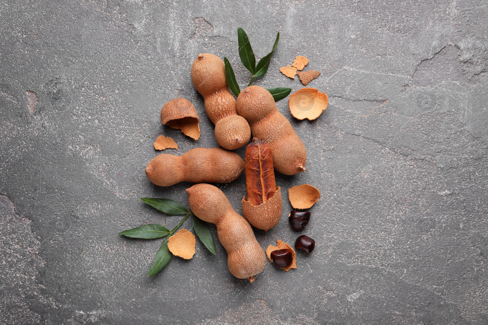 Photo of Ripe tamarinds and fresh leaves on grey table, flat lay