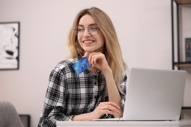 Photo of Woman with credit card using laptop for online shopping at white table indoors