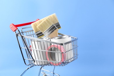 Photo of Small shopping cart with set of painting tools on light blue background