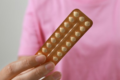 Photo of Woman holding birth control pills on grey background, closeup
