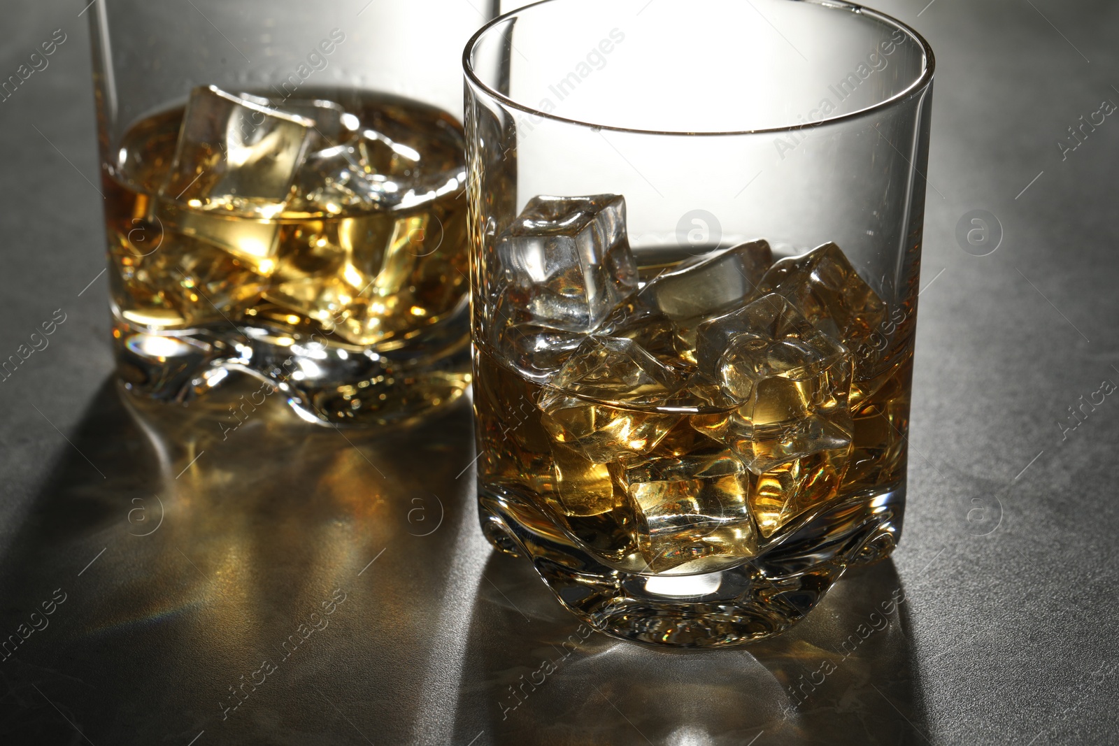 Photo of Whiskey with ice cubes in glasses on grey table, closeup