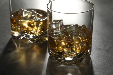 Photo of Whiskey with ice cubes in glasses on grey table, closeup