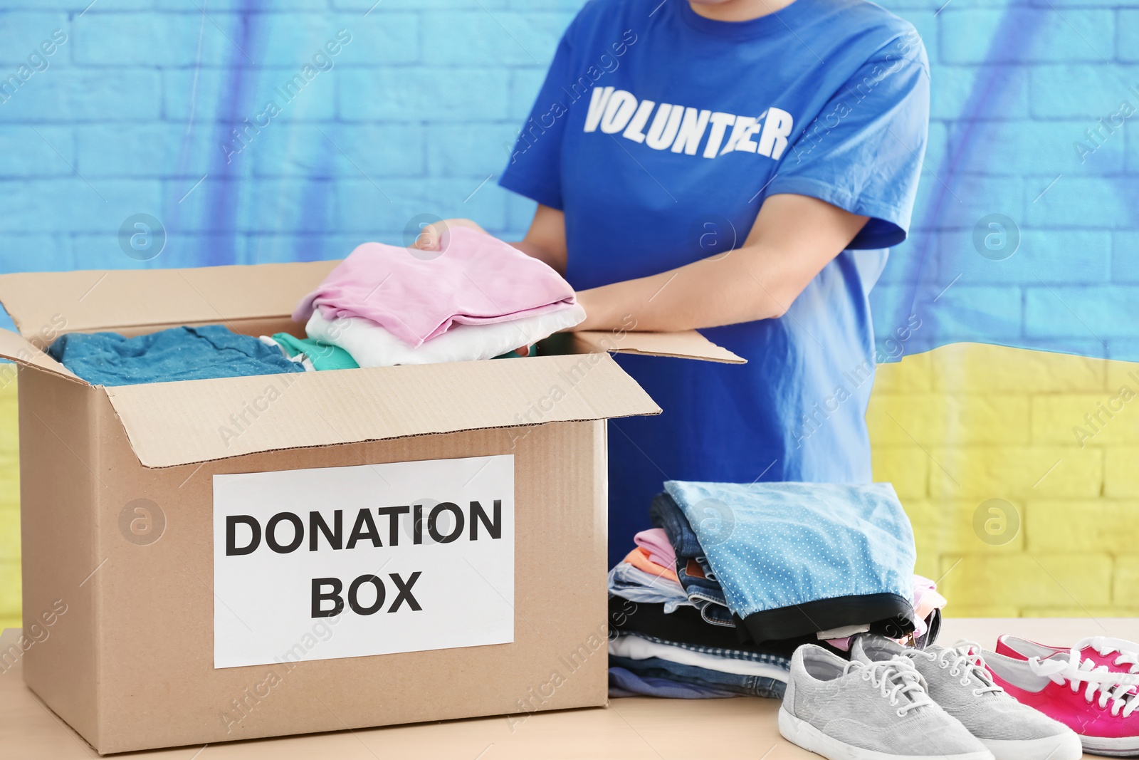 Image of Volunteer packing clothes and shoes in donation box at table with Ukrainian flag on background. Help during war