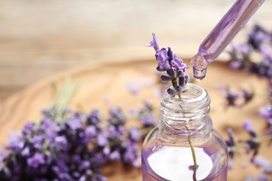 Photo of Natural oil dripping into bottle and lavender flowers on table, closeup with space for text. Cosmetic product