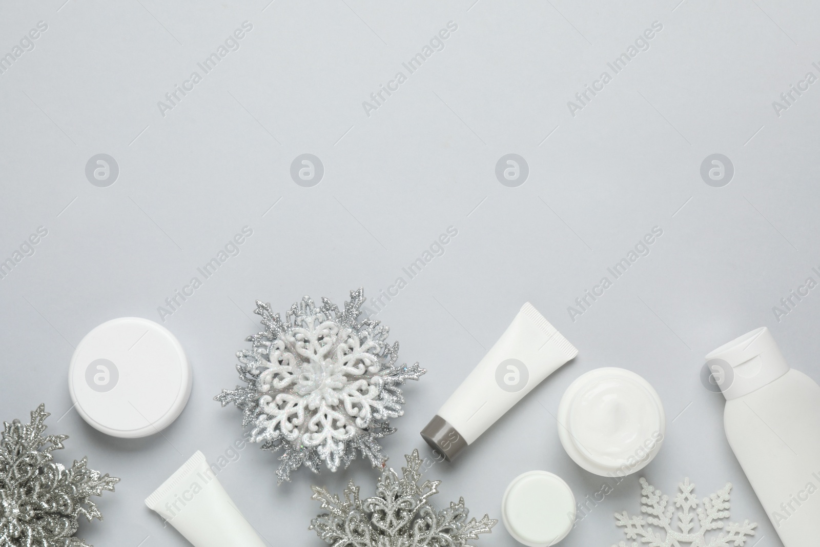 Photo of Flat lay composition with cosmetic products and snowflakes on light grey background, space for text. Winter skin care