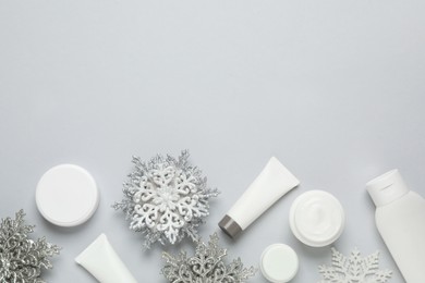 Flat lay composition with cosmetic products and snowflakes on light grey background, space for text. Winter skin care