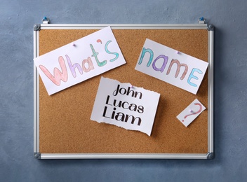 Cork board with baby names hanging on grey wall