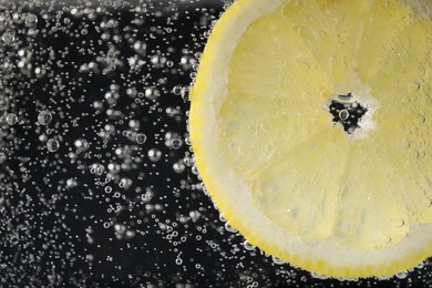 Photo of Juicy lemon slice in soda water against black background, closeup. Space for text