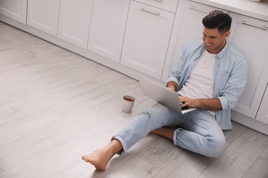 Photo of Man with laptop sitting on warm floor in kitchen, space for text. Heating system