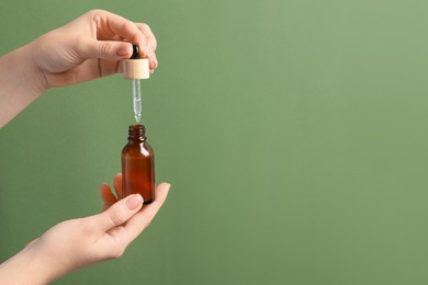 Photo of Woman dripping serum from pipette into bottle against olive background, closeup. Space for text