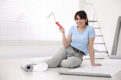 Photo of Woman with roller and wallpaper in room