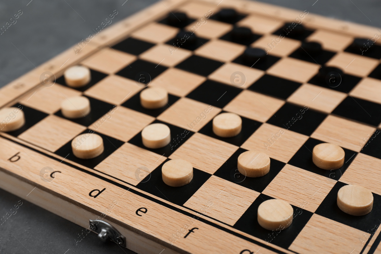 Photo of Wooden checkerboard with game pieces on grey table, closeup