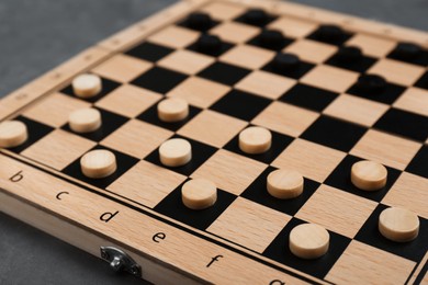 Photo of Wooden checkerboard with game pieces on grey table, closeup