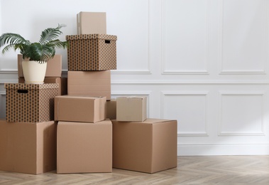 Photo of Heap of cardboard boxes and houseplant near white wall indoors, space for text. Moving day