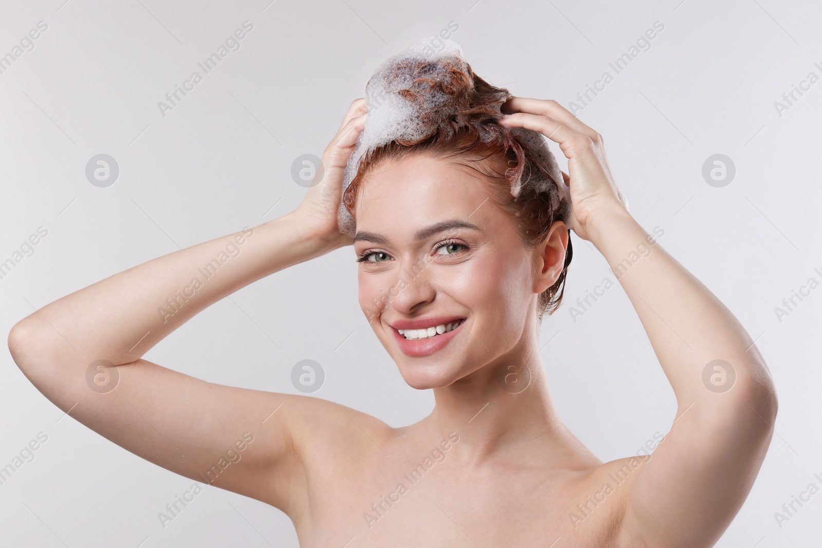 Photo of Happy young woman washing her hair with shampoo on light grey background